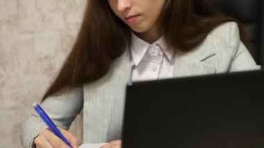 Sekreter kalem not defterinde yazıyor. dizüstü bilgisayar ve alır notlarda ofiste sandalyede oturan kız. belgili tanımlık laptop çalışan genç kadın girişimci.