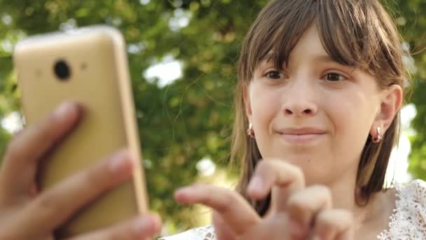 Chica joven charlando en una tableta con amigos. hermosa muchacha escribe en el smartphone la carta en el parque en primavera, el verano. Chica adolescente mira a través de fotos en un teléfono inteligente en un banco. comprobar correo electrónico en línea . — Vídeo de stock