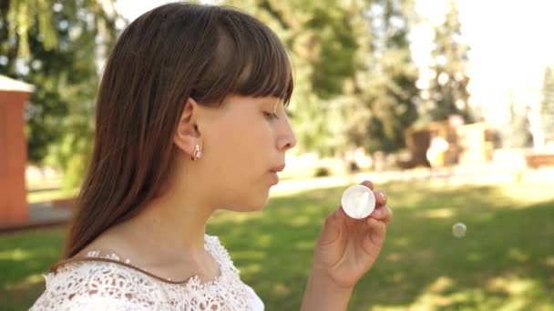 Щаслива дівчина дме красиві мильні бульбашки в парку навесні, влітку і посміхається. Повільний рух. молода дівчина подорожує містом у парку . — стокове відео