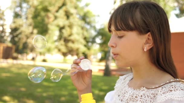 Gelukkig meisje mooi zeepbellen blazen in het park in de lente, zomer en glimlachen. Slow-motion. jong meisje reizen door de stad in het park. — Stockvideo
