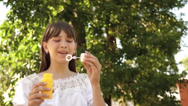 Menina feliz soprando belas bolhas de sabão no parque na primavera, verão e sorrindo. Movimento lento. menina viajando pela cidade no parque . — Vídeo de Stock