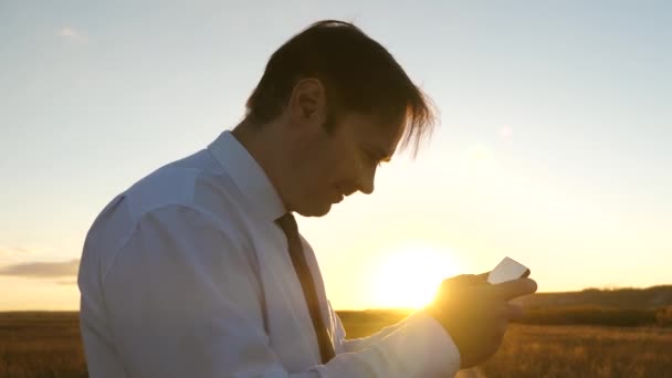 Obchodník s tabletovým zápasem v parku v teplých paprscích zapadajícího slunce. člověk hraje hry na telefonu. šťastný muž v bílé košili a kravatě hraje on-line na tabletu. — Stock video