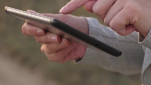 ビジネスウーマンは電子メールをチェックします。ユーシュカスの指は、タブレットを横切って自分の指を導きます。公園の夕暮れ時にタブレットで働くビジネスウーマン。フィールドでタブレットを操作するアグロノミスト. — ストック動画