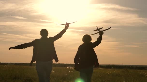 Дети негодяи на фоне солнца с самолетом в руке. Две девушки играют с игрушечным самолетом на закате. Силуэт детей, играющих в самолете. Мечтает летать. Концепция детских игр — стоковое видео