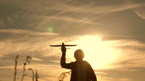 El niño corre al sol con un avión en la mano. Silueta de niños jugando en el avión. chica jugando con un avión de juguete al atardecer. Sueños de volar. El concepto de una infancia feliz . — Vídeos de Stock