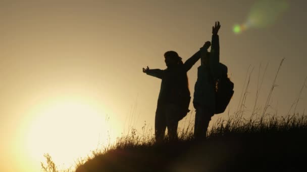 Hiker Girl Levantando la mano, celebrando la victoria y disfrutando del paisaje. mamá y su hija de vacaciones viajando y bailando en la montaña. Mujer con las manos levantadas en la cima de la montaña mirando el atardecer . — Vídeos de Stock