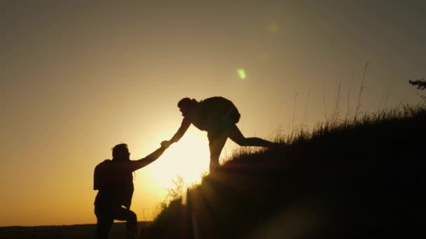 Woman traveler stretches a hand to a man climbing to the top of a hill. travelers climb the cliff holding hands. teamwork of business people. Happy family on vacation. tourists hug on top of mountain — Stock Video