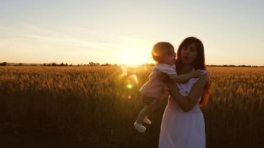 Anne ve bebek yaz alanında yürür. seyahat anne ve çocuk. mutlu aile kavramı. Küçük kızıyla genç bir anne, güzel bir gün batımının ışınlarıyla, buğday tarlasında dans ediyor ve gülüyor..