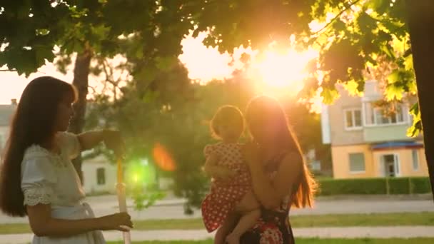 Мама і її дочки зловити великий і прозорий мильні бульбашки в міському парку і сміх в відблиски сонця — стокове відео