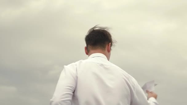 Businessman in suit launches toy with paper flying airplane against background of dark clouds — Stock Video