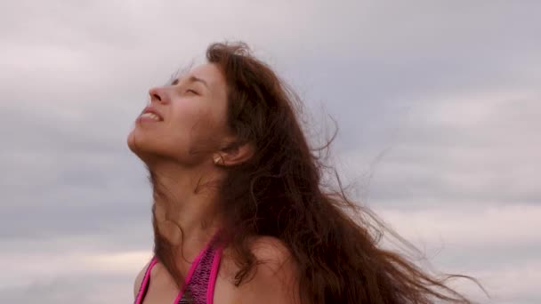 Flicka med utveckla långt hår ler mot mörka himmel. Kvinnan promenader i molnigt väder i kväll. Närbild — Stockvideo