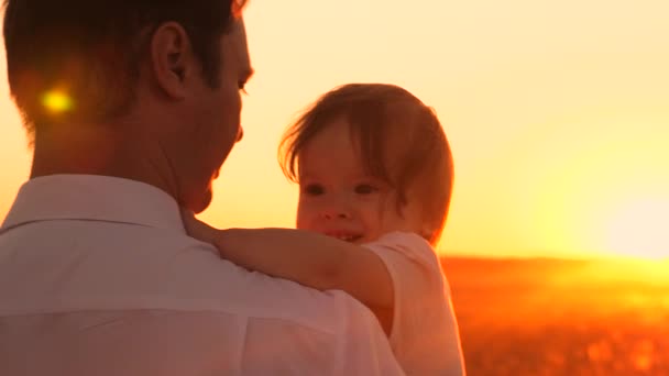 Тато тримає в руках маленьку дитину. Батько грає з дитиною на сонці. командна робота тато і дочка. щасливий тато гуляє зі своєю маленькою донькою в сільській місцевості. сім'я відпочиває в парку на заході сонця . — стокове відео