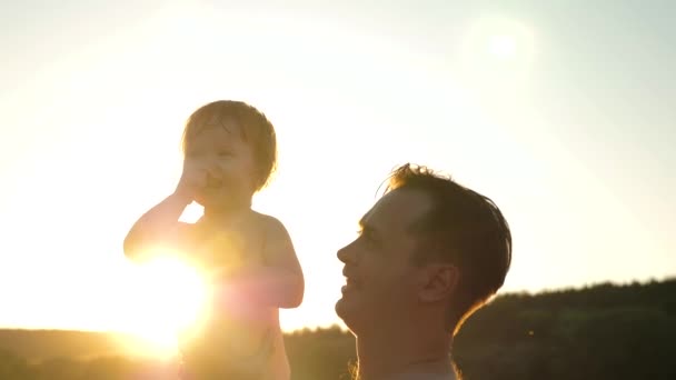 Feliz família na praia. O pai brinca com a filha. O bebé e o pai estão a nadar na água. Pai feliz e bebê sorridente alegre, banhar-se e brincar na água no por do sol dourado. pai e filho trabalho em equipe — Vídeo de Stock