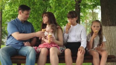 parkta yürüyen mutlu bir aile. çocuklar ve ebeveynler. Ebeveynleri olan çocuklar bankta oturmuş dondurma yiyip gülüyorlar. Mutlu aile