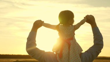 baba gün batımı ışınları nda omuzlarında kızı ile yürür. Babam sevgili çocuğunun omuzlarında, tarlada yürürken. Ebeveynleri olan bir bebek akşam gün batımında yürür. Yavaş çekim.