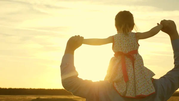 baba gün batımı ışınları nda omuzlarında kızı ile yürür. Babam sevgili çocuğunun omuzlarında, tarlada yürürken. Ebeveynleri olan bir bebek akşam gün batımında yürür. Yavaş çekim.