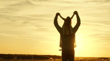 Babamın omuzlarında güneşte kızı ile dans ediyor. Baba gün batımı ışınları içinde omuzlarında bebek ile seyahat ediyor. Ebeveynleri olan bir çocuk gün batımında yürür. mutlu aile parkta istirahat. Aile konsepti