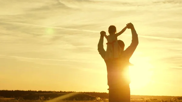 Papà danzava sulle spalle con sua figlia al sole. Papà viaggia con il bambino sulle spalle in raggi di tramonto. Un bambino con i genitori cammina al tramonto. famiglia felice che riposa nel parco. concetto di famiglia — Foto Stock