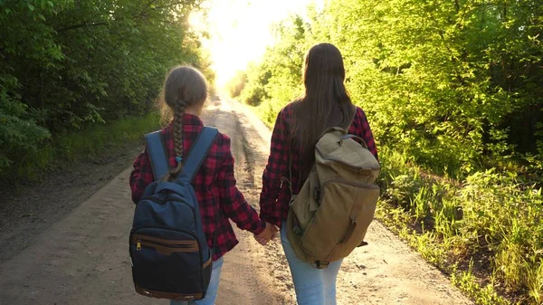 Wanderin. Mädchen sind mit Rucksäcken auf einer Landstraße unterwegs. Touristinnen gehen zum Sonnenuntergang. glückliche Familie auf Urlaubsreisen. Sporttourismuskonzept. — Stockfoto