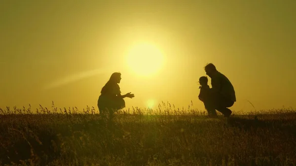 Matka a tatínek si hrají se svou dcerou na slunci. šťastné dítě chodí od táty k mámě. mladá rodina v terénu s dítětem 1 rok. koncept rodinného štěstí. krásné slunce, západ slunce. — Stock fotografie
