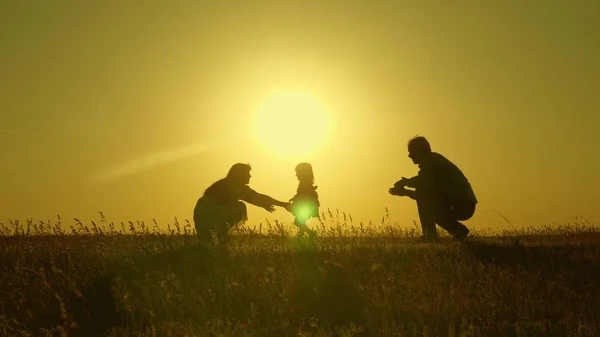 Mamá y papá juegan con su hija al sol. bebé feliz va de papá a mamá. familia joven en el campo con un niño de 1 año. concepto de felicidad familiar. hermoso sol, puesta de sol . — Foto de Stock