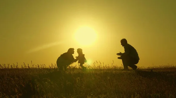 Mamá y papá juegan con su hija al sol. bebé feliz va de papá a mamá. familia joven en el campo con un niño de 1 año. concepto de felicidad familiar. hermoso sol, puesta de sol . —  Fotos de Stock