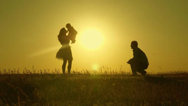 Maman et papa jouent avec leur fille au soleil. bébé heureux va de papa à maman. jeune famille sur le terrain avec un enfant 1 an. concept de bonheur familial. beau soleil, coucher de soleil . — Photo