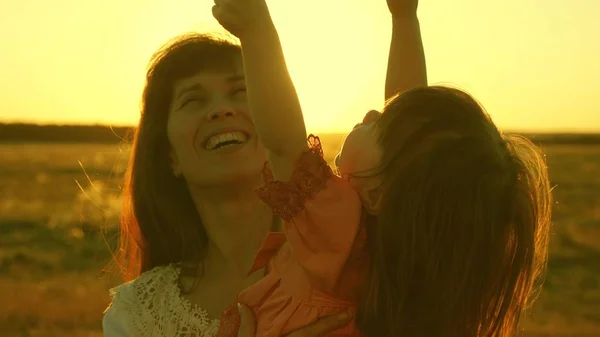 Feliz madre camina con su hija en sus brazos en los rayos del atardecer. Mamá está hablando con el bebé feliz, el bebé está sentado en los brazos de las madres al atardecer del sol dorado. Movimiento lento . —  Fotos de Stock