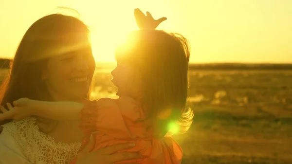 快乐的母亲在夕阳的光线下，抱着女儿散步。妈妈正在和快乐的宝宝说话，宝宝在金色的阳光下坐在妈妈的怀里。慢动作. — 图库照片