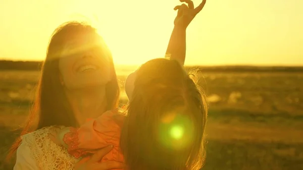 Madre felice cammina con la figlia tra le braccia nei raggi del tramonto. La mamma sta parlando con il bambino felice, il bambino è seduto sulle braccia delle madri al tramonto del sole dorato. Rallentatore . — Foto Stock