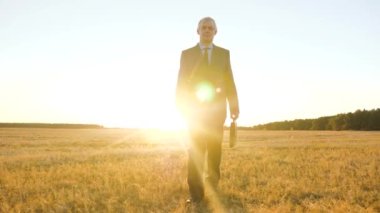 iş adamı güneşin içinde parkta yürür. Bir çiftçi tarlanın karşısına geçiyor. siyah evrak çantası ile iş adamı parlak güneş ışınları alanında yürüyüş.
