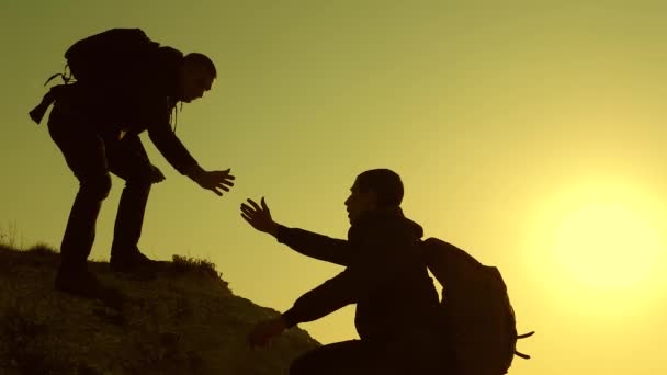 Os viajantes escalam um após o outro na rocha. trabalho de equipa de pessoas de negócios. Alpinistas silhuetas esticar as mãos um para o outro, subindo para o topo da colina. Uma equipe de empresários vai — Vídeo de Stock