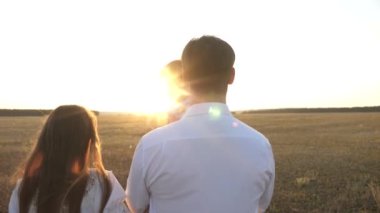 Babam ve annem kızı ile gün batımında kollarında yürüyebilir. gün batımında bir çocukla aile yürüyüşleri. Kız parkta dinlenmek ile baba. mutlu aile ve çocukluk konsepti.