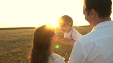 Baba ve annem gün batımında kollarında küçük bir kız ile oynuyor. gün batımında bir çocukla aile yürüyüşleri. Babası parkta dinlenirken kızları ile oynuyor. mutlu aile ve çocukluk konsepti.