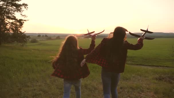 Kinderen spelen speelgoed vliegtuig. tieners willen piloot en astronaut worden. Happy Girls lopen met speelgoed vliegtuig bij zonsondergang op veld. concept van een gelukkige kindertijd. Meisjes dromen van het vliegen en een piloot worden. — Stockvideo