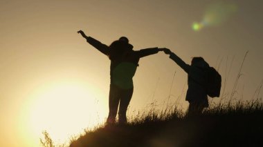 tatil seyahat ve dağda dans anne ve kızı. Dağın tepesinde, gün batımına bakarak yükseltilmiş elleri olan bir kadın. Hiker kız yetiştirmek onu el yukarı, kutluyor zafer ve zevk sahne.