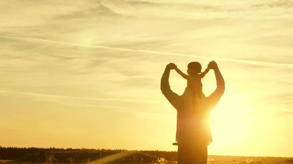 Papà danzava sulle spalle con sua figlia al sole. Papà viaggia con il bambino sulle spalle in raggi di tramonto. Un bambino con i genitori cammina al tramonto. famiglia felice che riposa nel parco. concetto di famiglia — Foto Stock