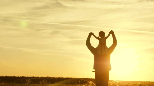 Papà danzava sulle spalle con sua figlia al sole. Papà viaggia con il bambino sulle spalle in raggi di tramonto. Un bambino con i genitori cammina al tramonto. famiglia felice che riposa nel parco. concetto di famiglia — Foto Stock