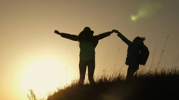 Mamma och dotter på semester resor och dans på berget. Kvinna med upphöjda händer på toppen av berget tittar på solnedgången. Vandrare flicka höja hennes hand upp, fira seger och njuta av landskap. — Stockfoto