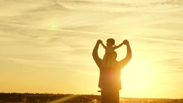 Papá bailando sobre sus hombros con su hija al sol. Padre viaja con el bebé sobre sus hombros en rayos de atardecer. Un niño con padres camina al atardecer. familia feliz descansando en el parque. concepto familiar — Vídeo de stock