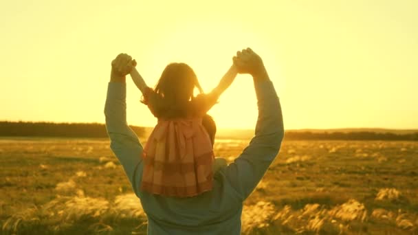 Papá bailando sobre sus hombros con su hija al sol. Padre viaja con el bebé sobre sus hombros en rayos de atardecer. Un niño con padres camina al atardecer. familia feliz descansando en el parque. concepto familiar — Vídeo de stock