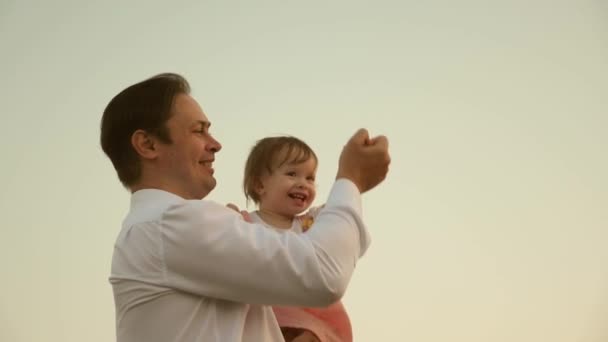 Papà danzava sulle spalle con sua figlia al sole. Papà viaggia con il bambino sulle spalle in raggi di tramonto. Un bambino con i genitori cammina al tramonto. famiglia felice che riposa nel parco. concetto di famiglia — Video Stock