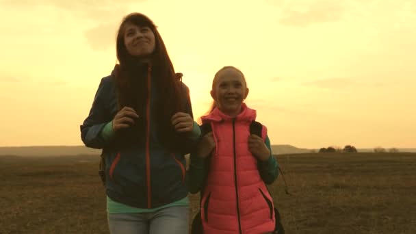 Touristes heureux maman et fille vont avec des sacs à dos sur la plaine. famille en vacances voyage. concept de tourisme sportif familial. Maman et enfant voyagent avec un sac à dos contre le ciel . — Video