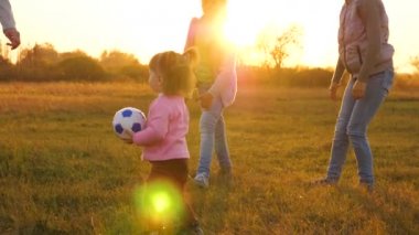 anne top küçük kızı ile oynar. Yavaş çekim. mutlu çocuk çim üzerinde topu ile çalışır, futbol topu atar. Gün batımında bir parkta çocuk topu tarafından küçük bir çocuk ile oynayan aile.