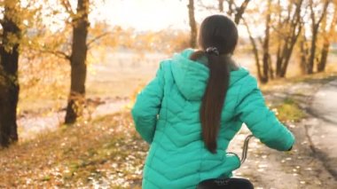 kız yolda bisikletle seyahat ediyor. bir bisiklet üzerinde sportif genç binmek. Yeşil ceketli genç bir kız sonbahar parkına giden yolda bisiklete biniyor..