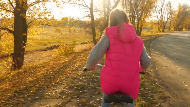 Çocuk yolda bisikletle seyahat eder. spor bir bisiklet genç kız yürümek. Kırmızı ceketli genç bir kız sonbahar parkına giden yolda bisiklete biniyor.. — Stok video