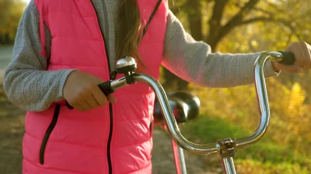 Chica rueda una bicicleta y sostiene las manos rueda curva. niño viaja en bicicleta en el camino. deportes caminar adolescente chica en una bicicleta. Una joven con una chaqueta roja monta una bicicleta en el camino al parque de otoño . — Vídeo de stock