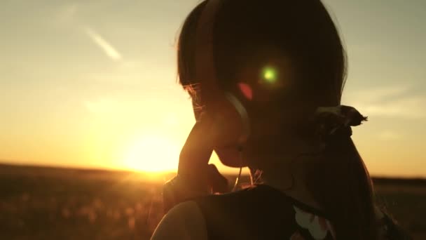 Teen girl listening to music and watching the sunset. Happy girl dancing in headphones in the rays of a beautiful sunrise in the park. young girl dreams to music in the sun — Stock Video