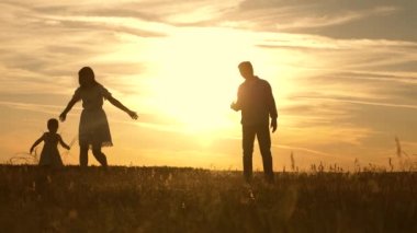 mutlu küçük kızı anne ve baba ile oynuyor. ebeveynlerle oynayan mutlu çocuk. Anne ve baba gün batımında parkta çocuk oynarken, çocuk ilk adımları alır.