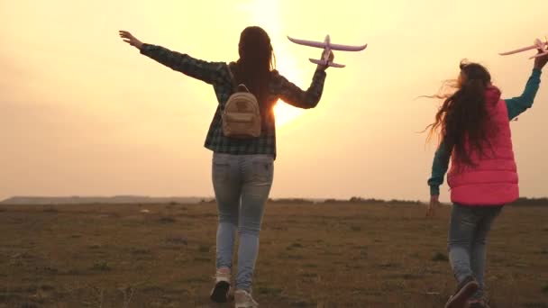 Niños juegan juguete avión. Los adolescentes quieren convertirse en pilotos y astronautas. Chicas felices corren con avión de juguete al atardecer en el campo. concepto de una infancia feliz. Las niñas sueñan con volar y convertirse en piloto . — Vídeo de stock